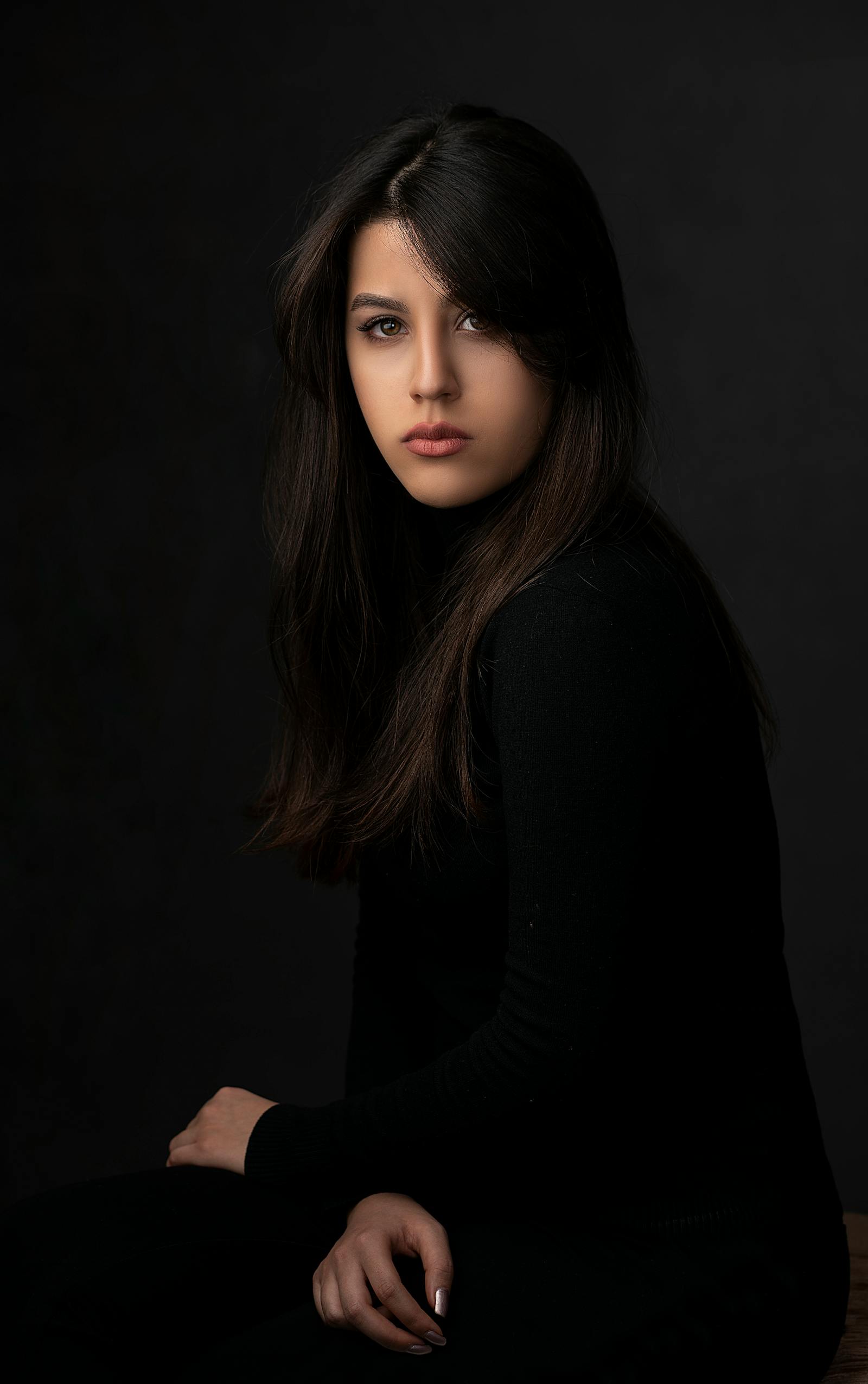 A studio portrait lit in warm tungsten — a young woman in profile against a deep charcoal seamless, soft fall-off on her shoulder, signature Brivon lighting.